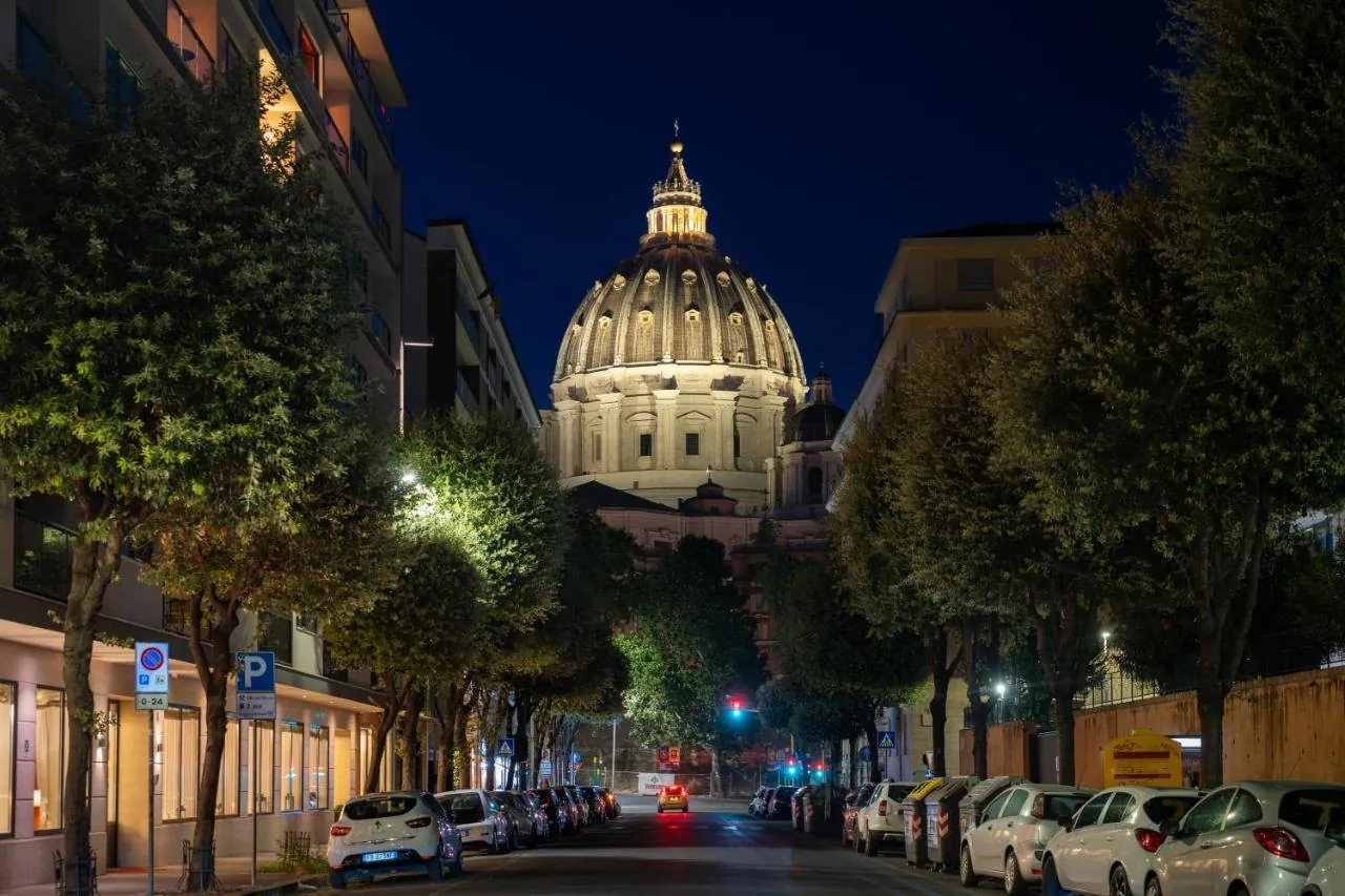 Una strada alberata di sera, con la cupola di San Pietro illuminata sullo sfondo